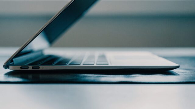 A sleek modern silver laptop centered on a dark desk mat against a clean soft gradient background