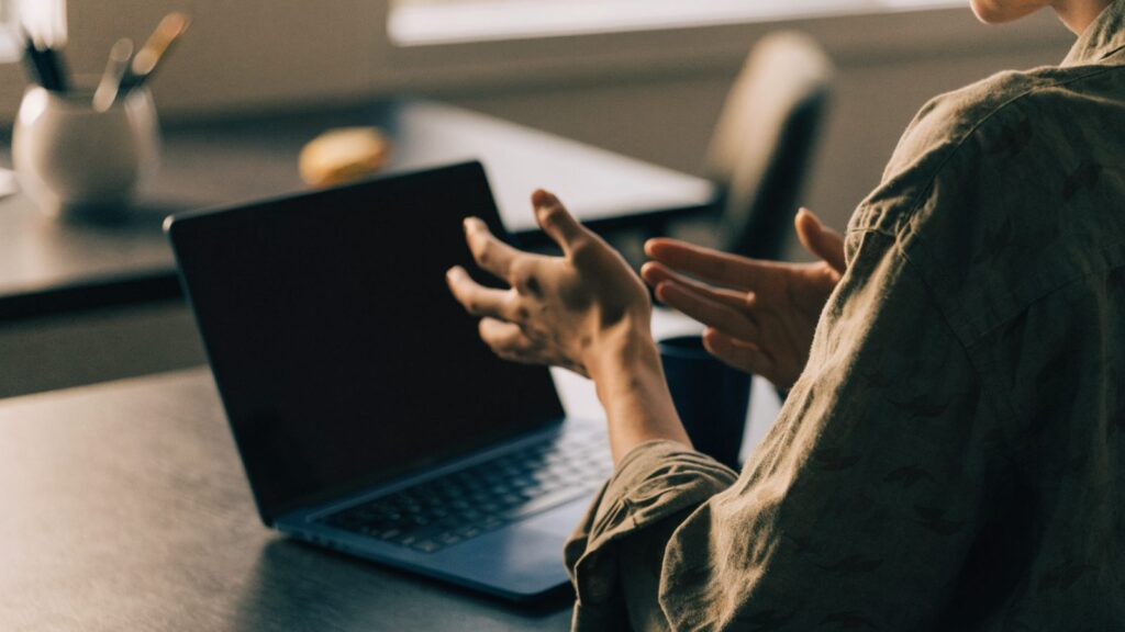 A person seen from behind with hands raised at a dark blue laptop with a dark blank screen on an office desk
