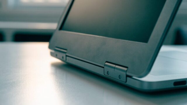 Close-up of the hinge and screen edge of a matte grey laptop on a white desk