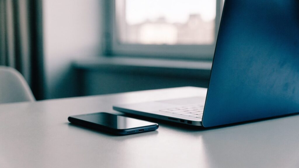A smartphone lying beside a dark blue laptop on a white desk