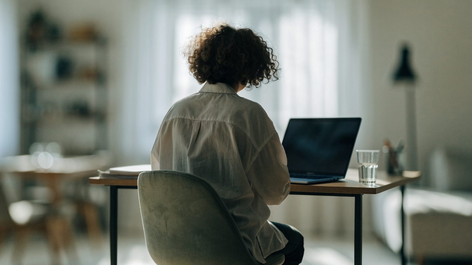 A person seen from behind working on a dark blue laptop in a bright home office