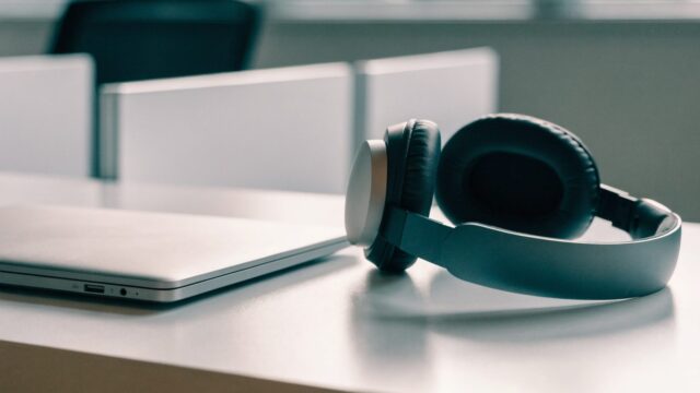 Over-ear headphones resting beside a silver laptop on a white desk