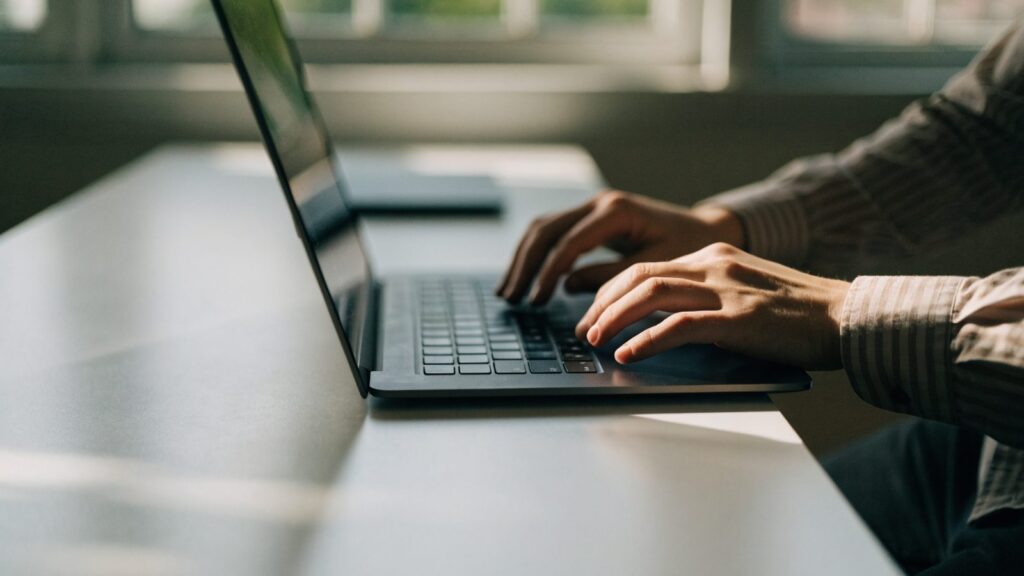 Hands typing on the keyboard of a graphite black laptop on a white desk