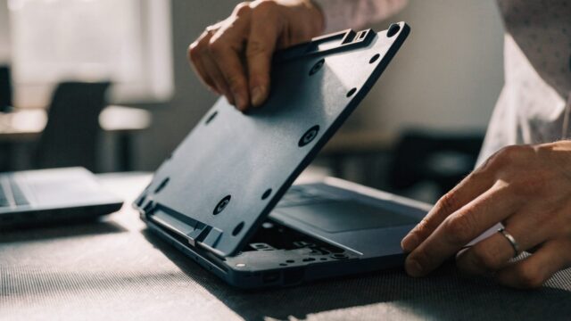 A technician lifting the bottom cover off a dark blue laptop on an anti-static mat