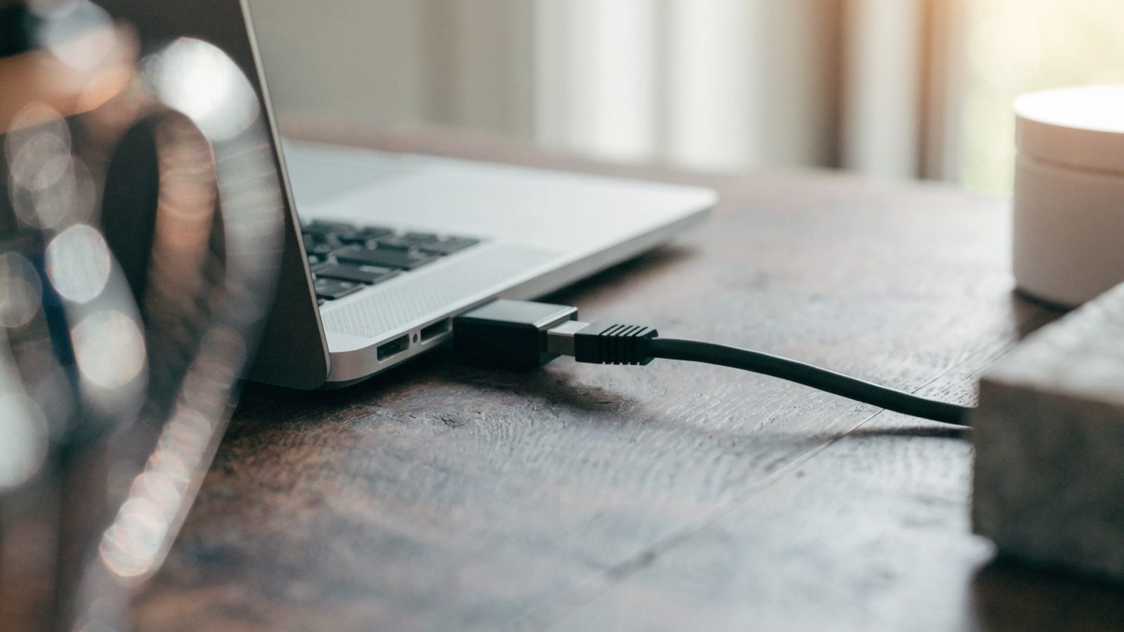 An ethernet cable being plugged into a USB-C adapter connected to a silver laptop on a workbench