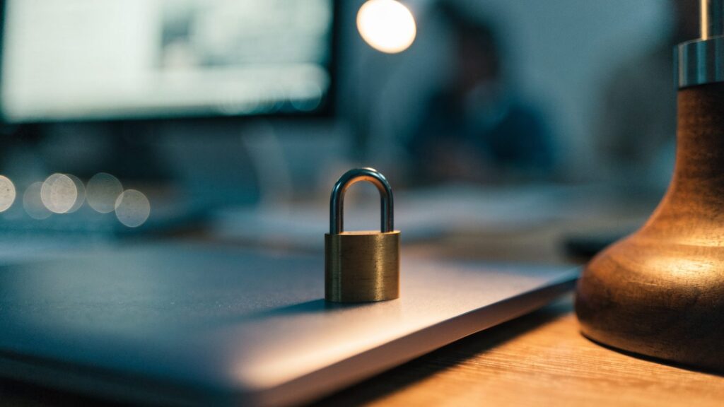 A small brass padlock resting on the closed lid of a dark blue laptop on an office desk