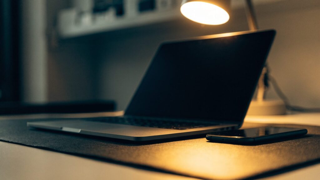 A smartphone lying beside a matte grey laptop on a dark desk mat