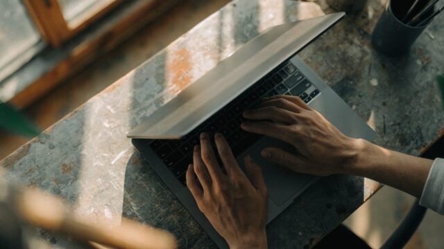 Hands typing on the keyboard of a matte grey laptop on a workbench