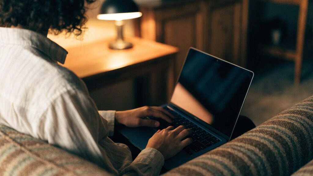 A person seen from behind using a dark blue laptop on a sofa