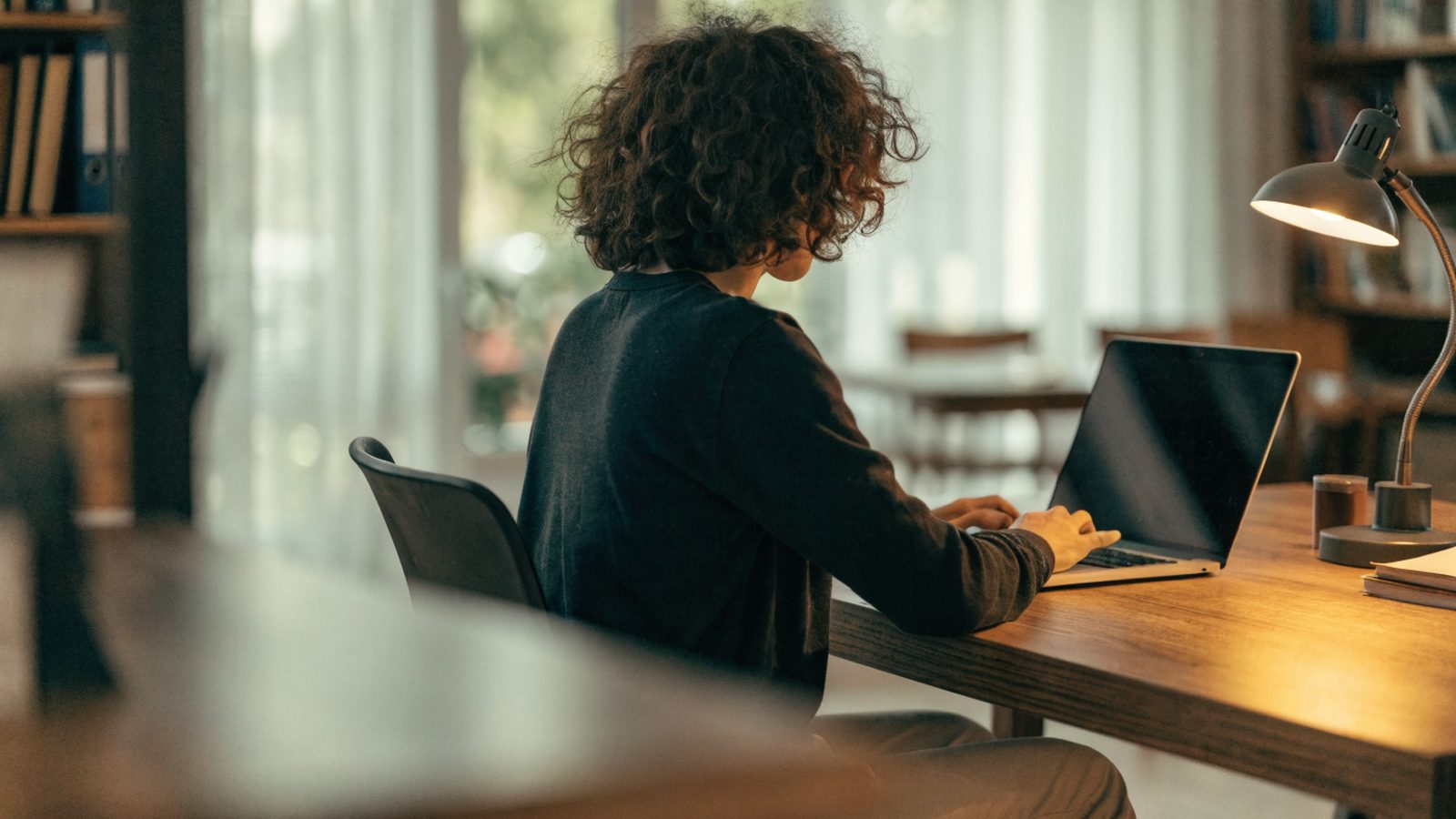A person seen from behind working on a silver laptop in a bright home office