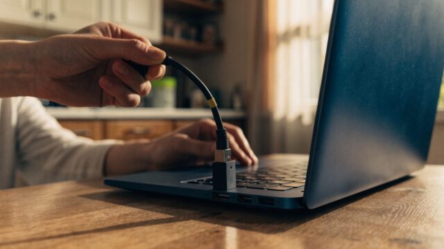An ethernet cable being plugged into a USB-C adapter connected to a dark blue laptop on a kitchen table
