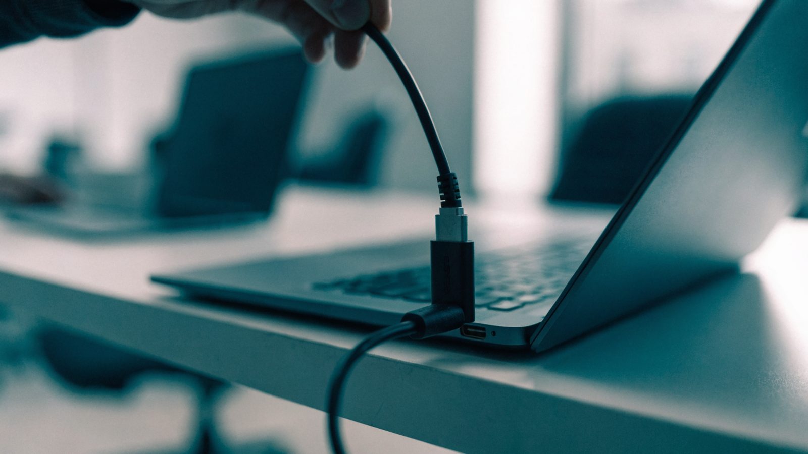 An ethernet cable being plugged into a USB-C adapter connected to a graphite black laptop on an office desk