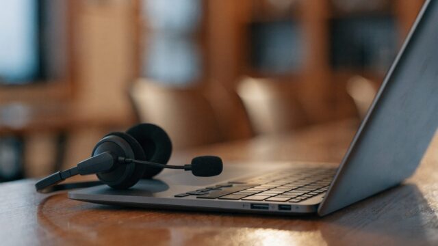 A USB headset with microphone plugged into a matte grey laptop on a wooden desk