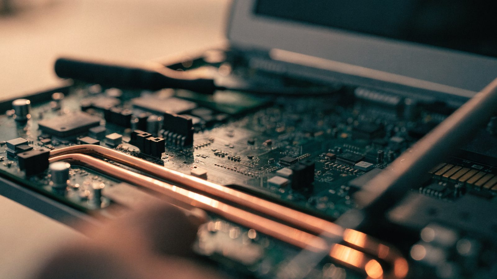 Close-up of a laptop motherboard with copper heat pipes during a repair