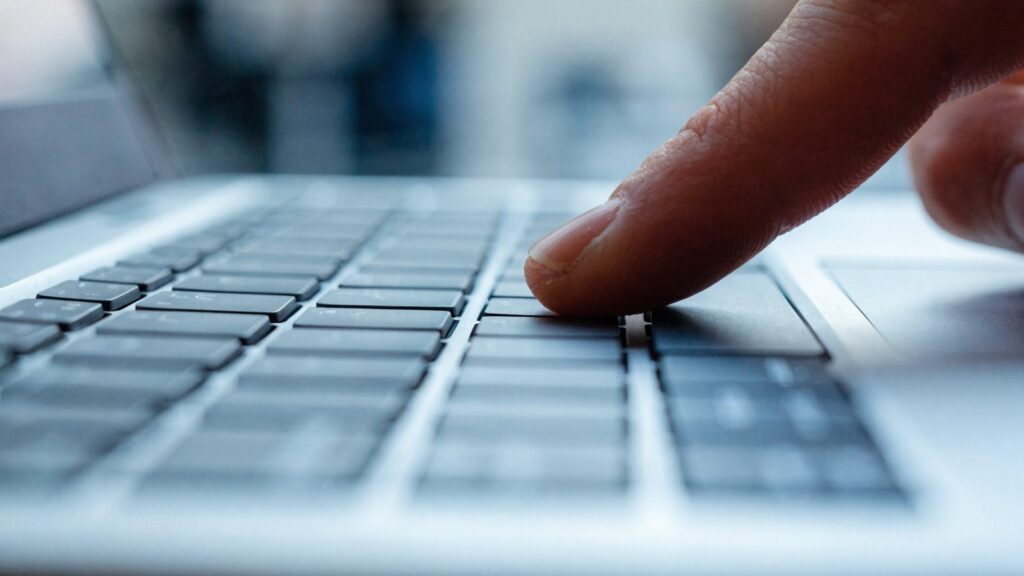 Close-up of a single key being pressed on a silver laptop keyboard
