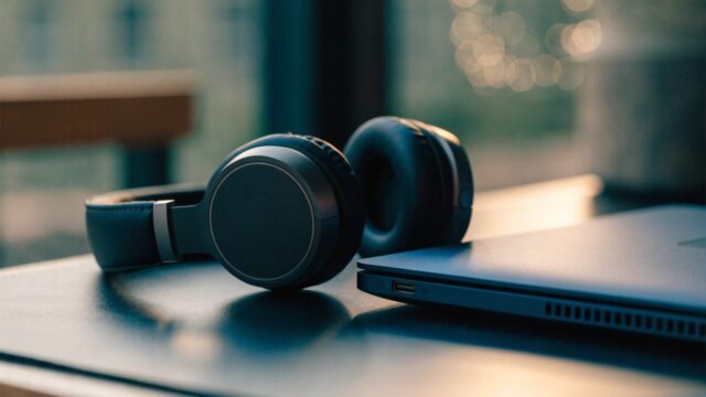 Over-ear headphones resting beside a dark blue laptop on a dark desk mat