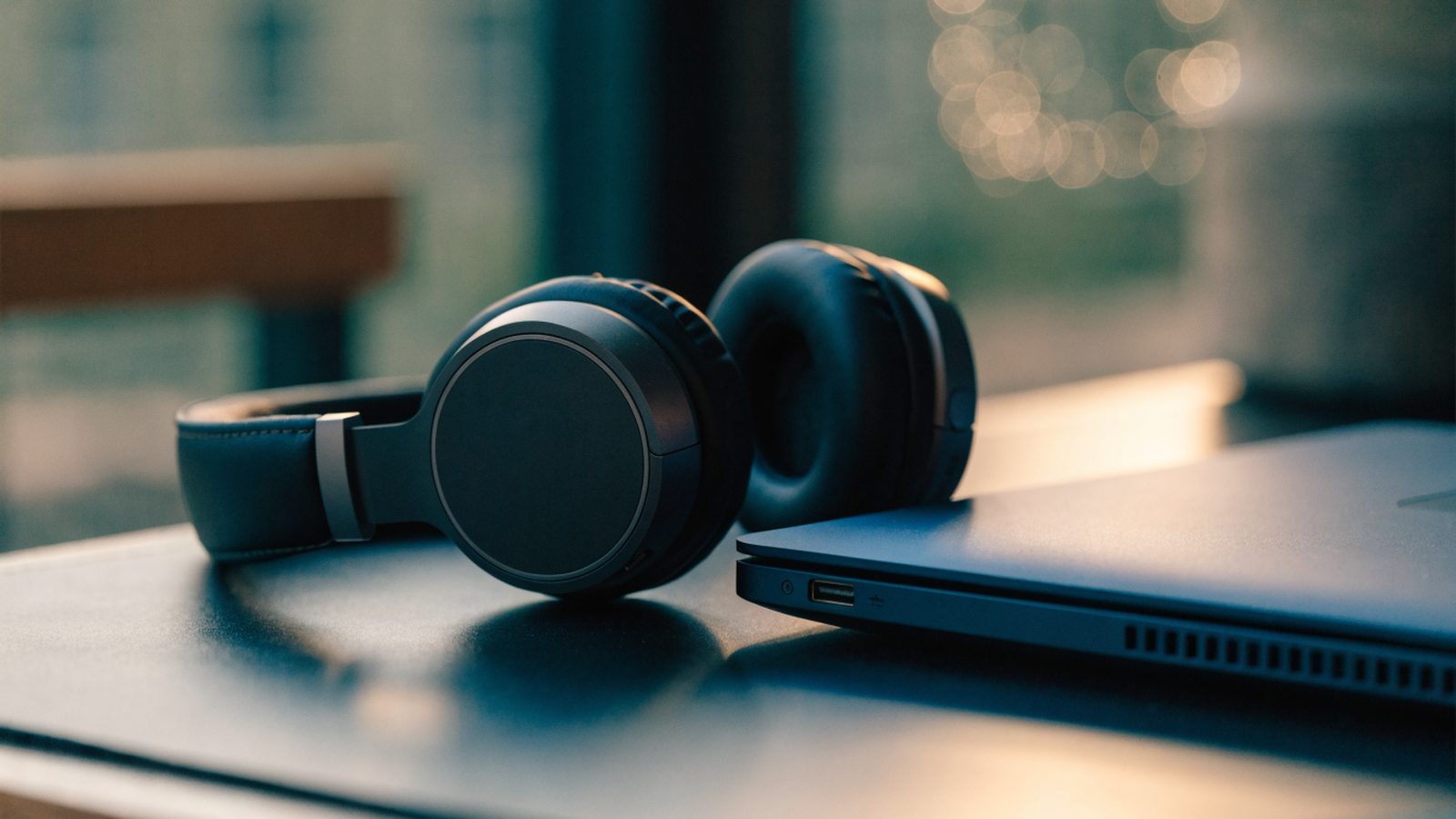 Over-ear headphones resting beside a dark blue laptop on a dark desk mat