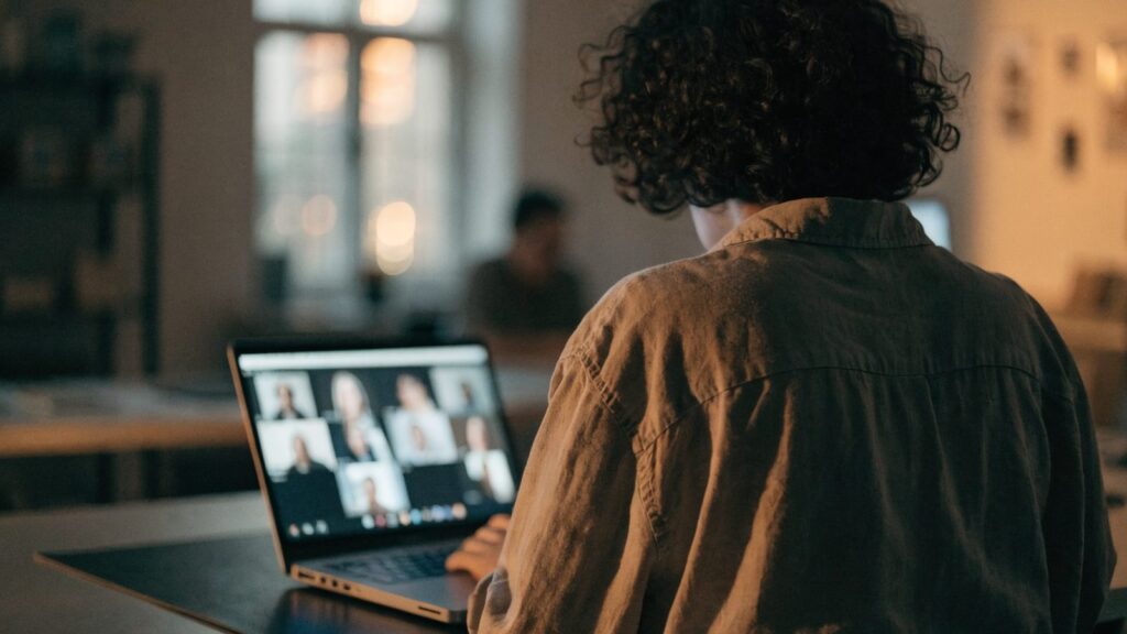 A person seen from behind on a video call on a matte grey laptop on a dark desk mat