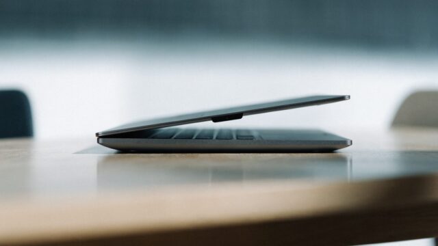 A sleek modern graphite black laptop centered on a wooden desk against a clean soft gradient background