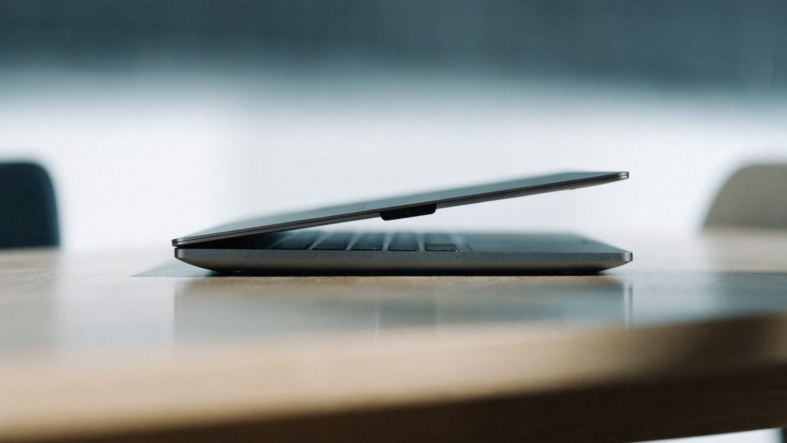 A sleek modern graphite black laptop centered on a wooden desk against a clean soft gradient background