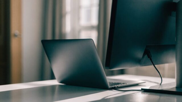 A graphite black laptop connected to a large external monitor with a blank dark screen via a cable on a white