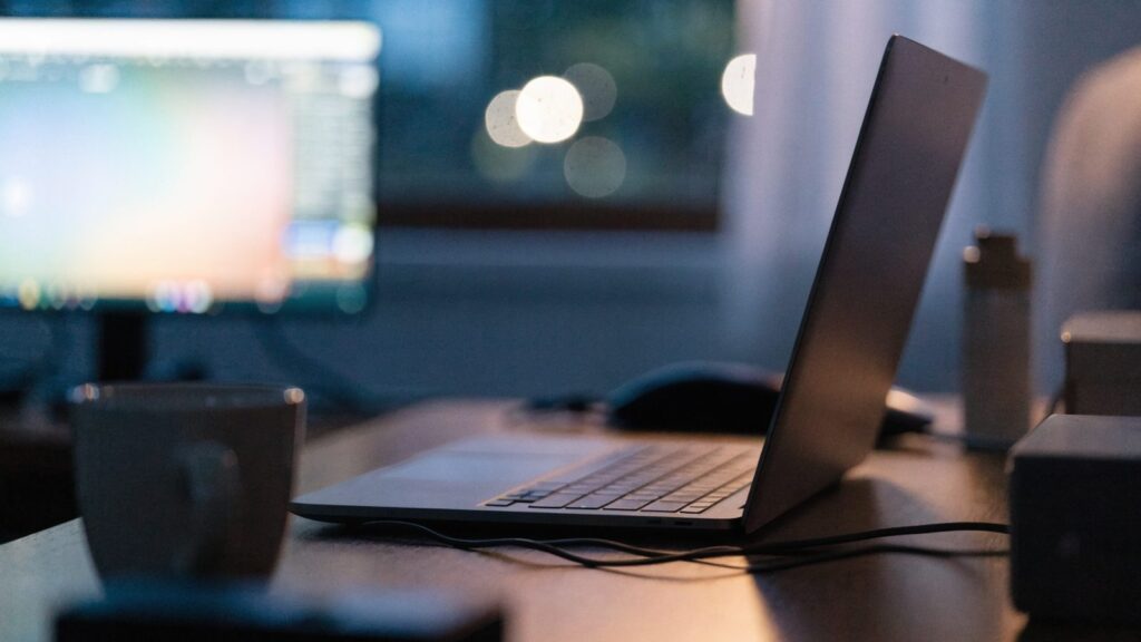 A developer's desk at night with a matte grey laptop and a second monitor showing soft blurred colorful glow