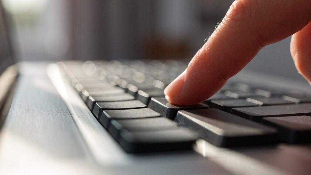 Close-up of a single key being pressed on a silver laptop keyboard