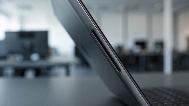 Close-up of the hinge and screen edge of a graphite black laptop on an office desk
