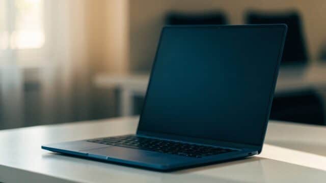 A dark blue laptop on a white desk with a completely dark blank screen