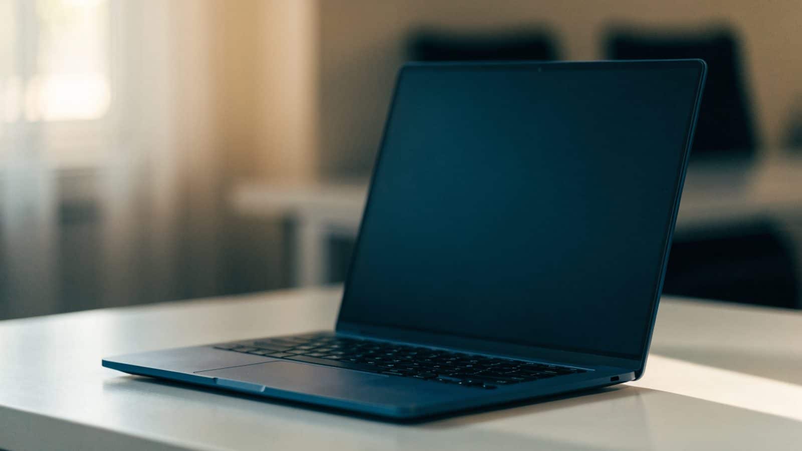 A dark blue laptop on a white desk with a completely dark blank screen