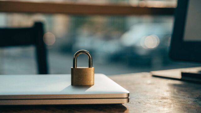 A small brass padlock resting on the closed lid of a silver laptop on a workbench