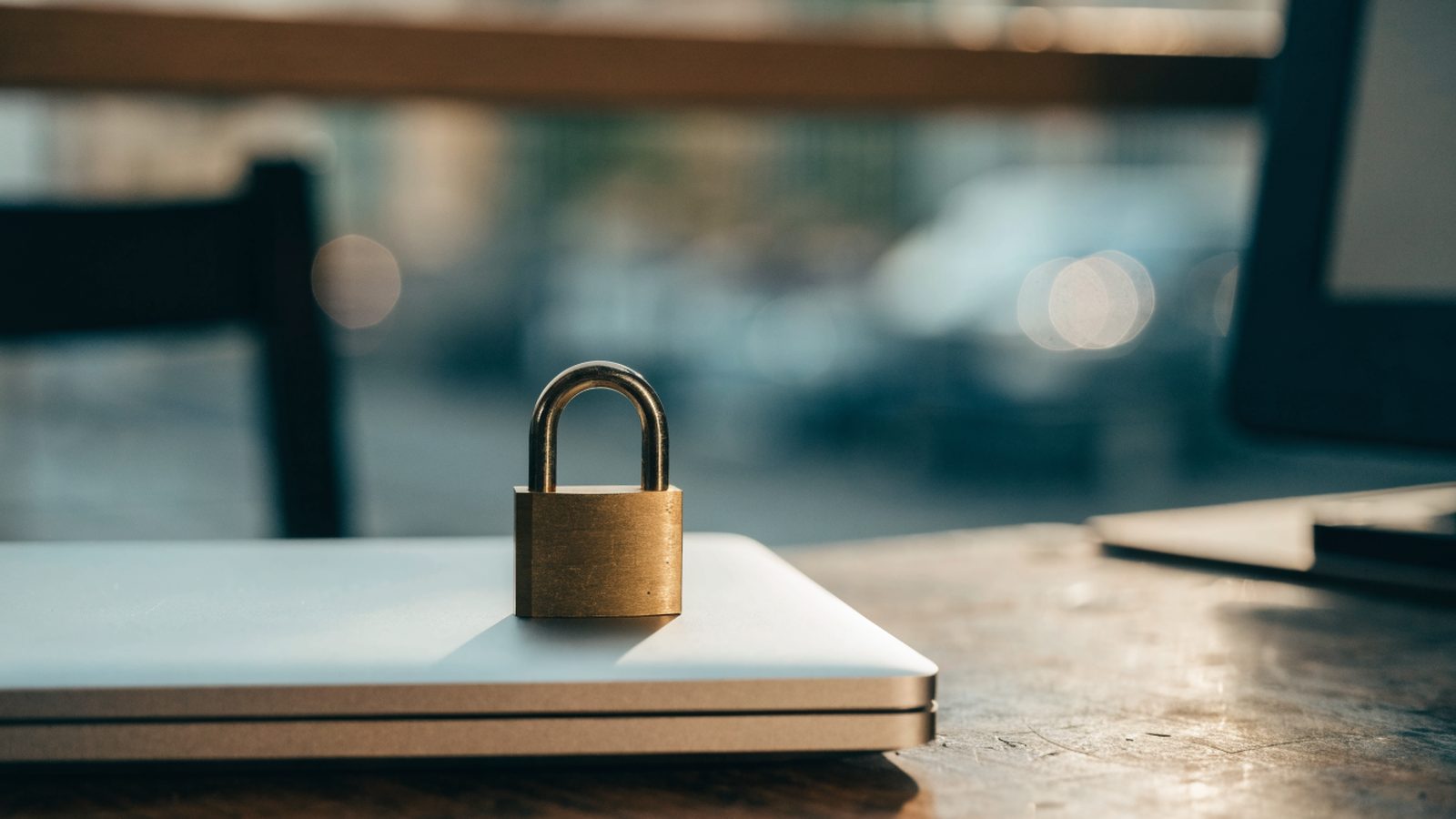 A small brass padlock resting on the closed lid of a silver laptop on a workbench