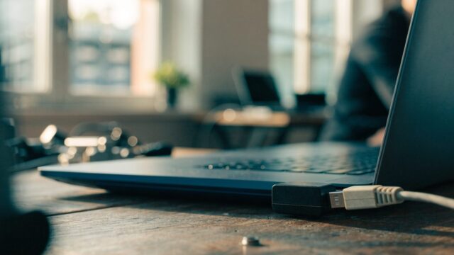 An ethernet cable being plugged into a USB-C adapter connected to a dark blue laptop on a workbench