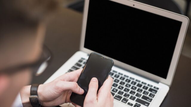 A businessman's hand using the mobile phone in front of laptop