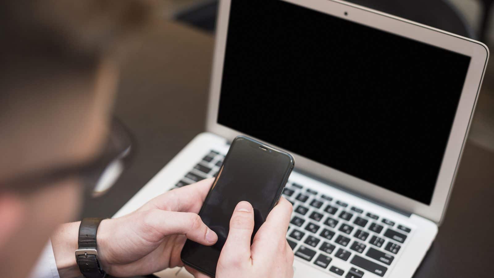 A businessman's hand using the mobile phone in front of laptop