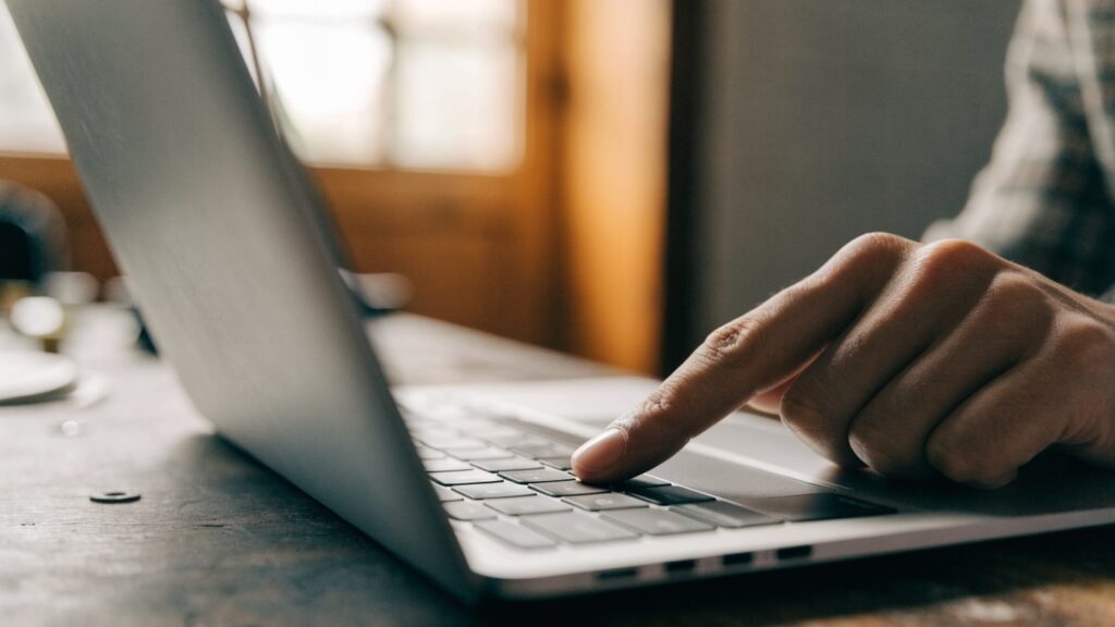 A finger gliding on the touchpad of a silver laptop on a workbench