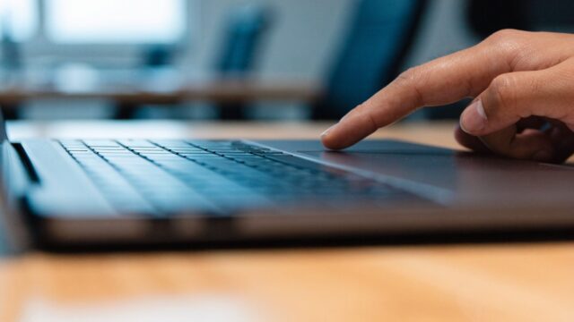 A finger gliding on the touchpad of a graphite black laptop on an office desk