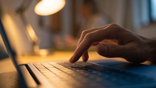 A finger gliding on the touchpad of a dark blue laptop on an office desk