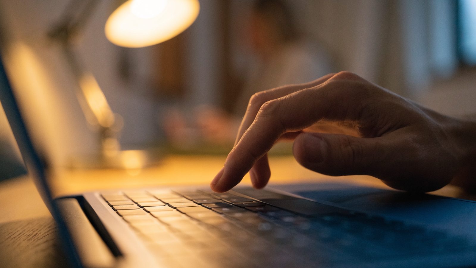 A finger gliding on the touchpad of a dark blue laptop on an office desk