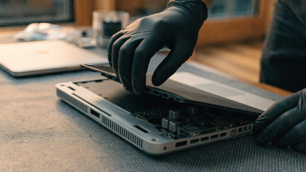 A technician lifting the bottom cover off a silver laptop on an anti-static mat