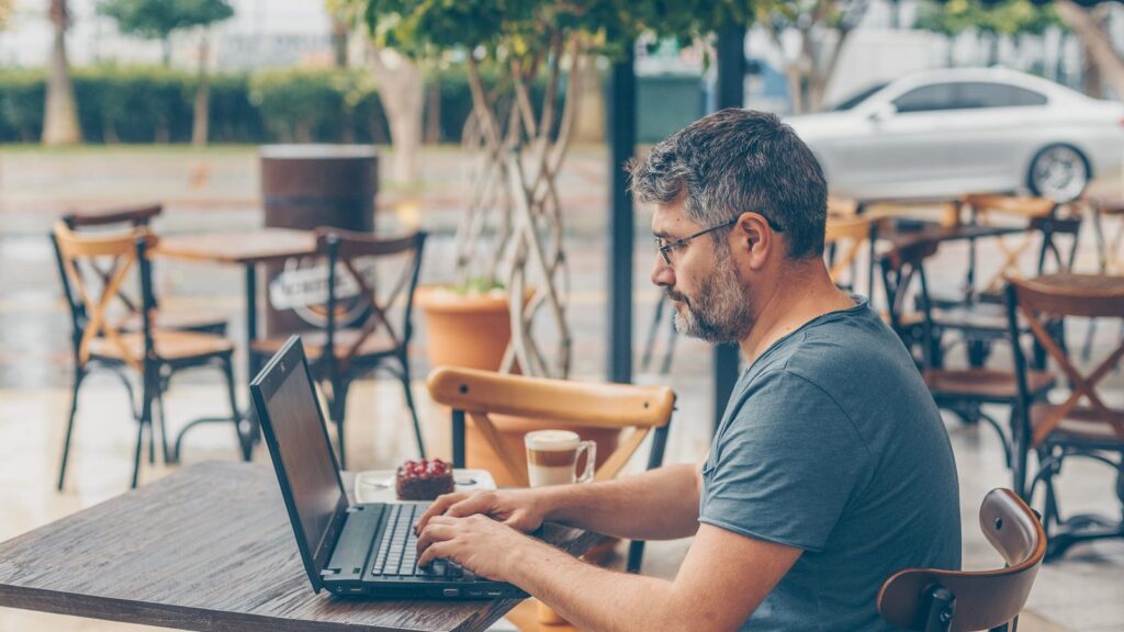 Man sitting and working on laptop in cafe terrace during daytime and looking busy