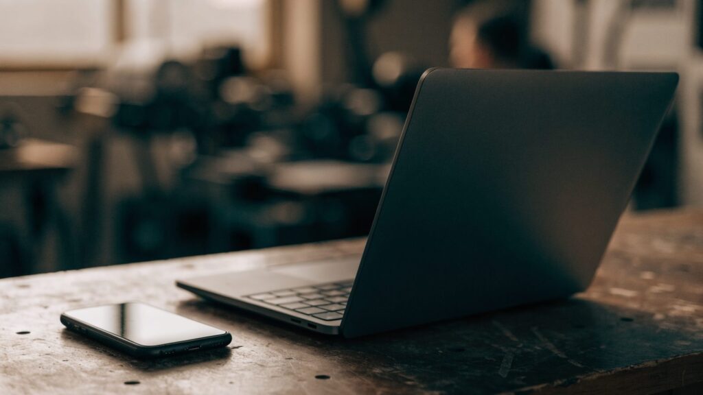 A smartphone lying beside a graphite black laptop on a workbench