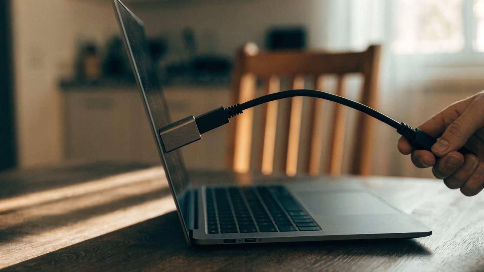 An ethernet cable being plugged into a USB-C adapter connected to a matte grey laptop on a kitchen table