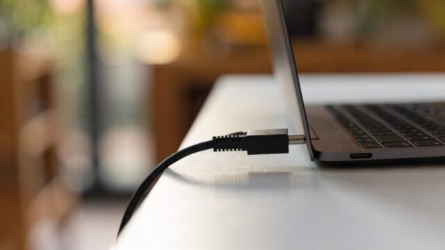 An ethernet cable being plugged into a USB-C adapter connected to a graphite black laptop on a white desk