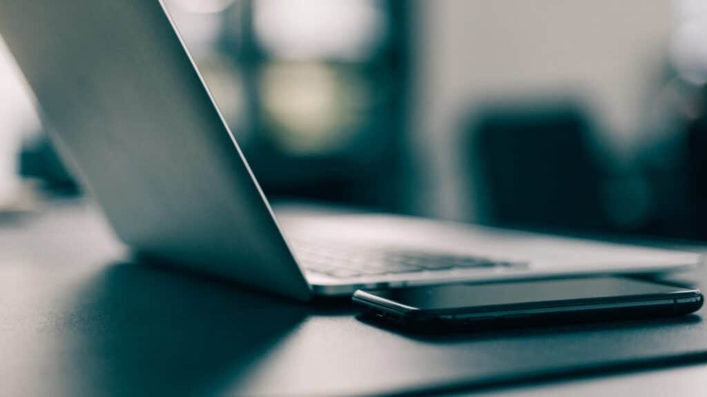 A smartphone lying beside a silver laptop on a dark desk mat