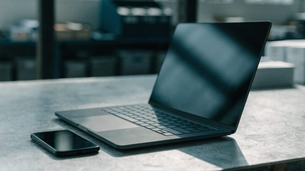 A smartphone lying beside a graphite black laptop on a workbench