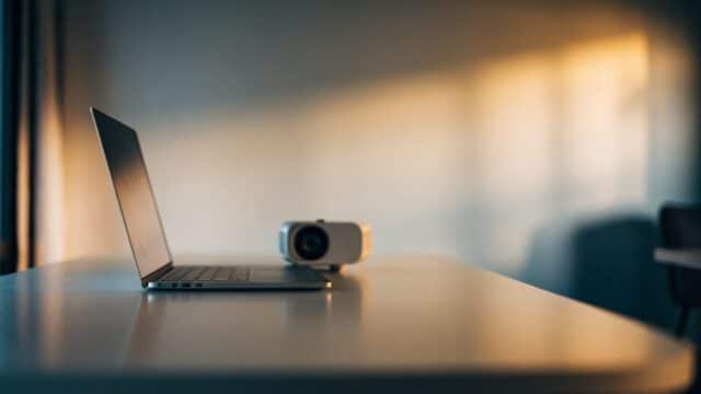 A silver laptop beside a small projector on a table
