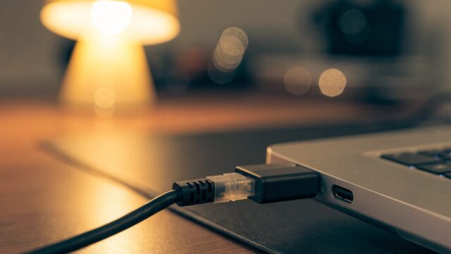 An ethernet cable being plugged into a USB-C adapter connected to a silver laptop on a dark desk mat