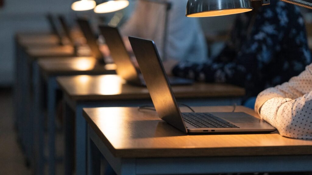 A row of laptops on desks in a school computer lab
