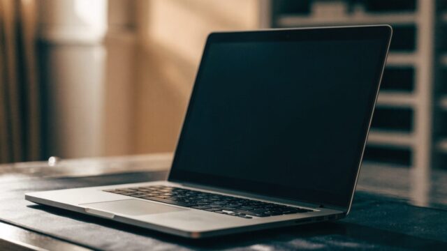 A silver laptop on a dark desk mat with a completely dark blank screen